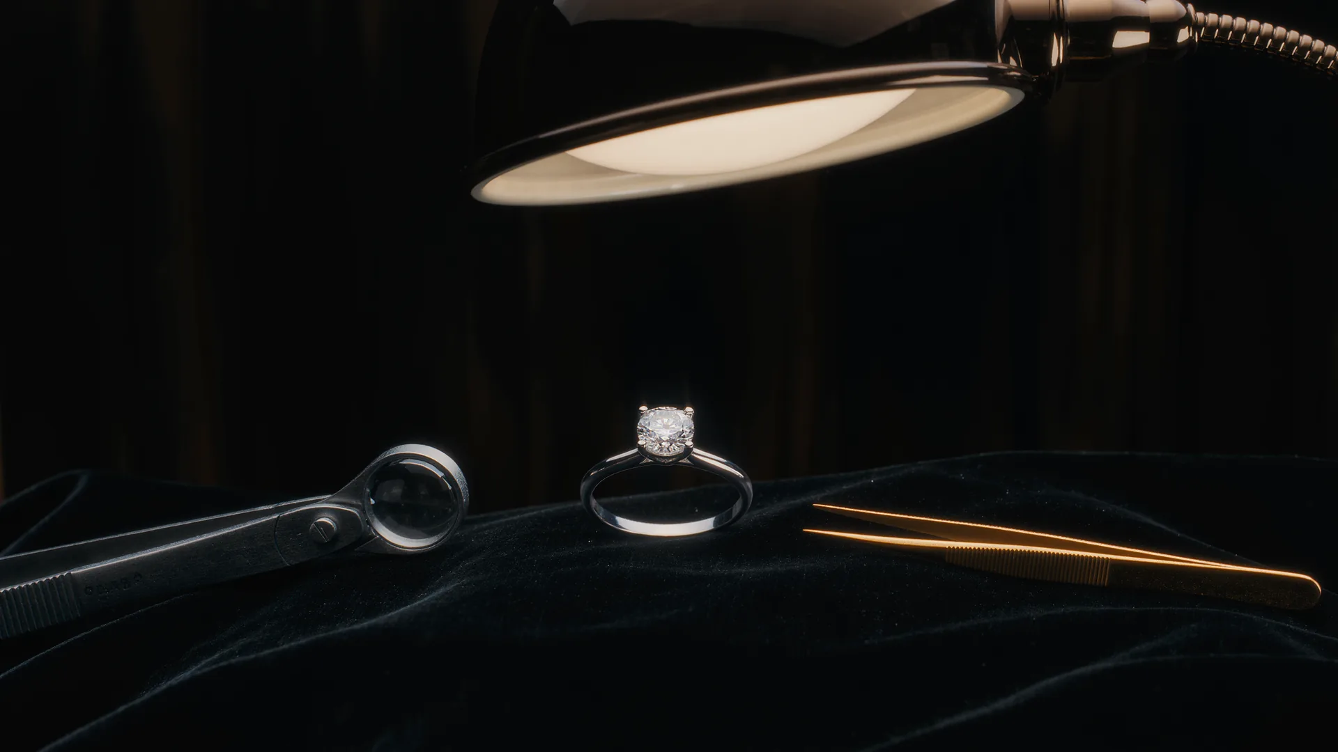 Diamond ring on black velvet under a jeweller's lamp, with loupe and tweezers