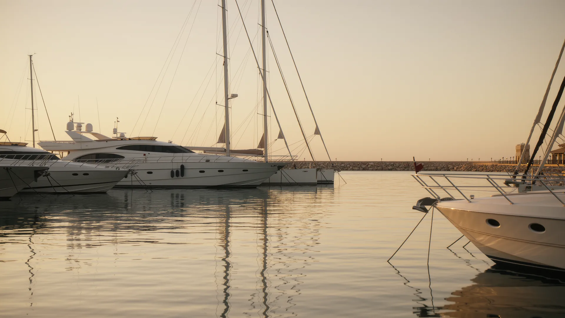 Marina with white hulls and masts at golden hour on calm water