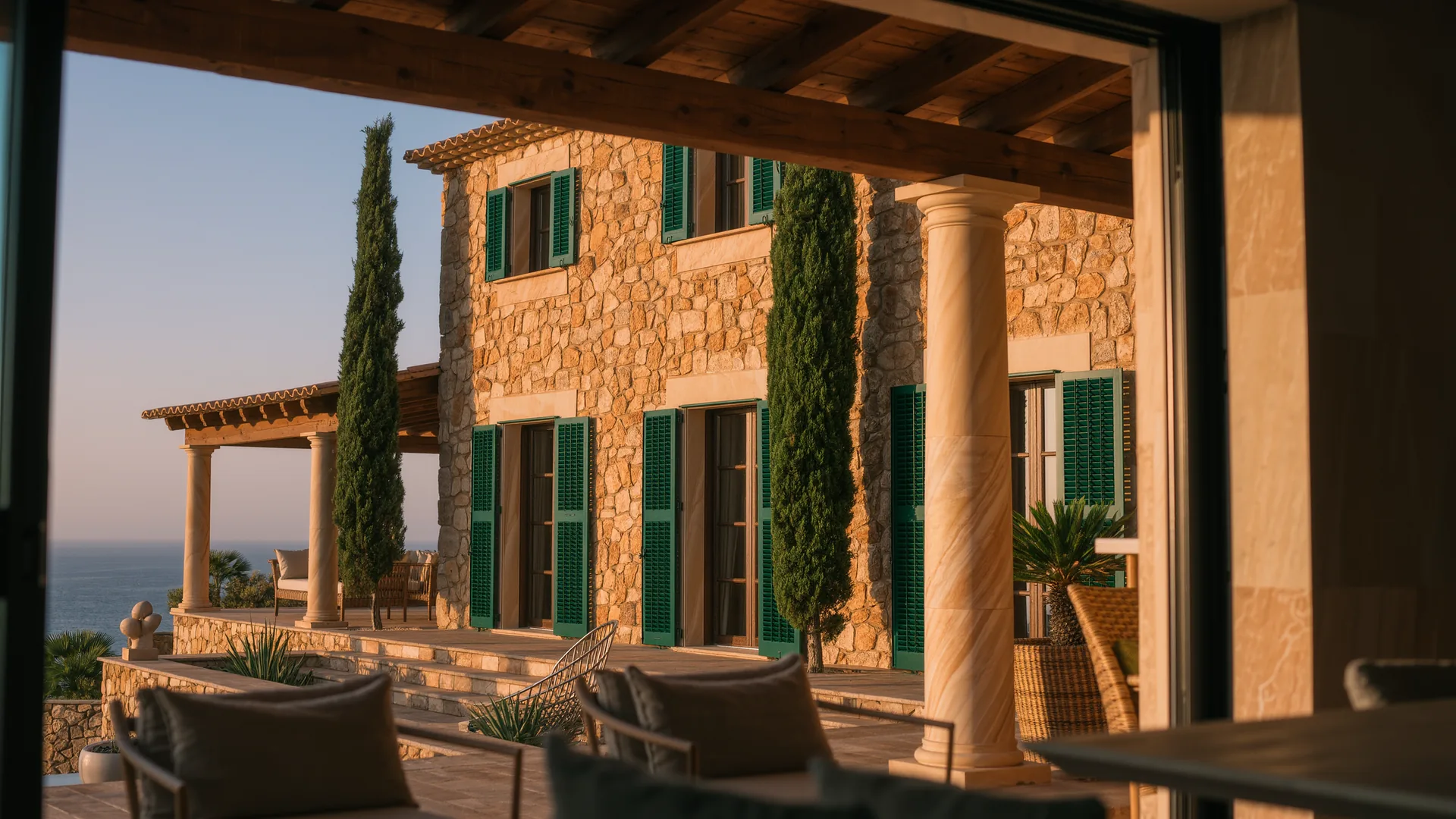 Mallorcan finca of honey coloured stone with green shutters and cypresses at golden hour