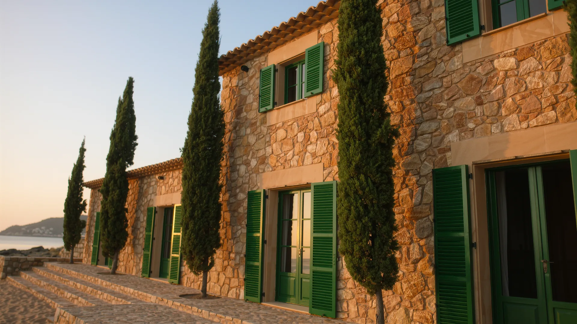 Mallorcan finca of honey coloured stone with green shutters and cypresses at golden hour