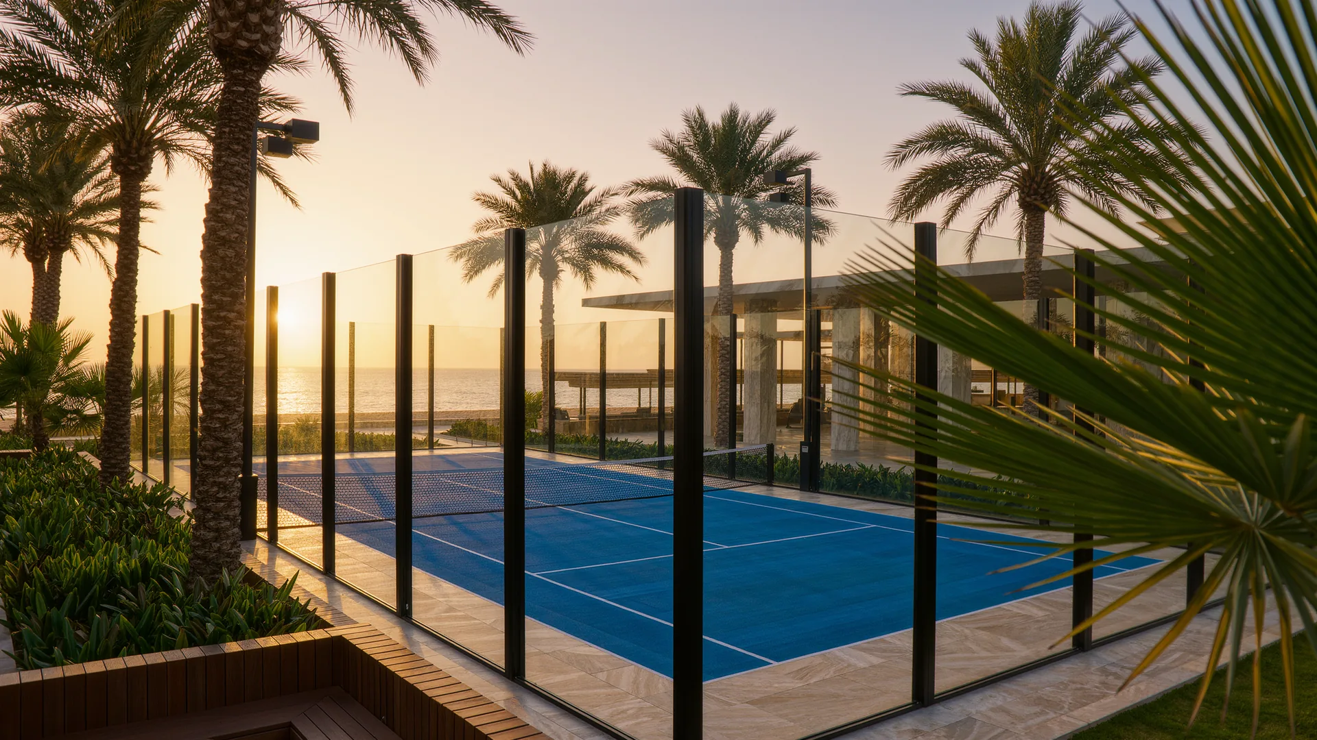 Padel court with glass walls and a blue surface among palm trees