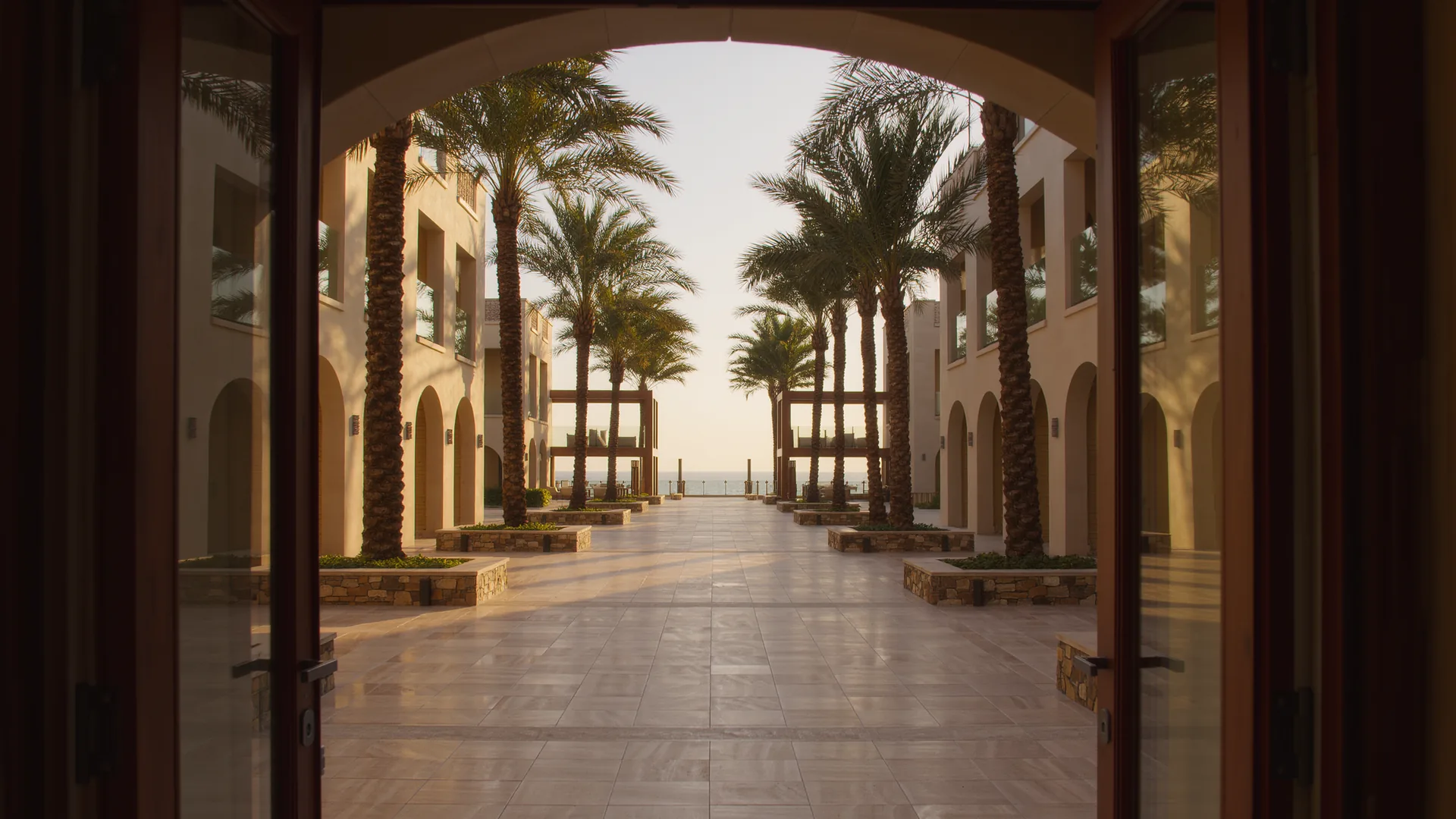 Apartment building courtyard with palms and a clean tiled walkway in morning light