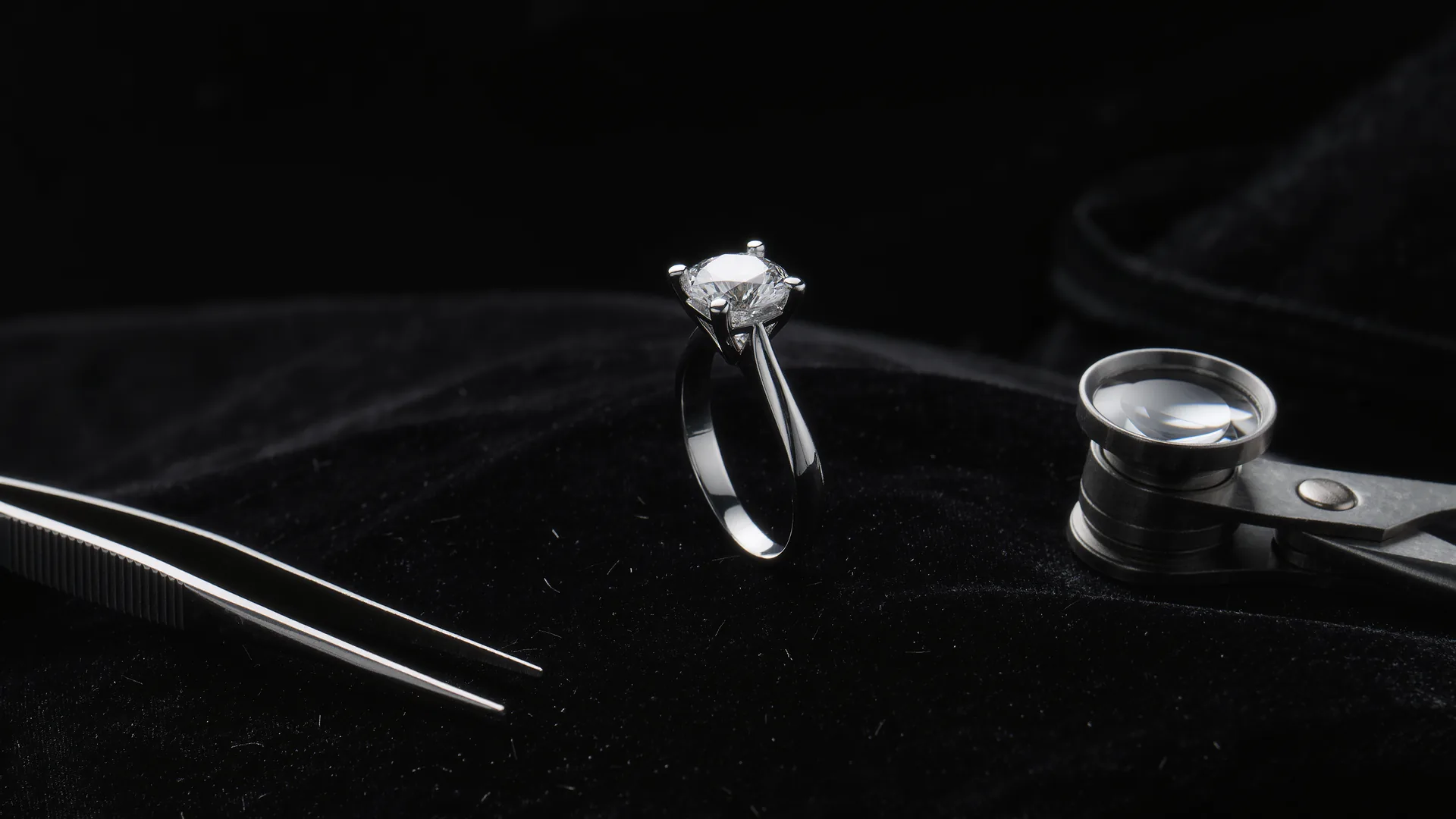 Diamond ring on black velvet under a jeweller's lamp, with loupe and tweezers
