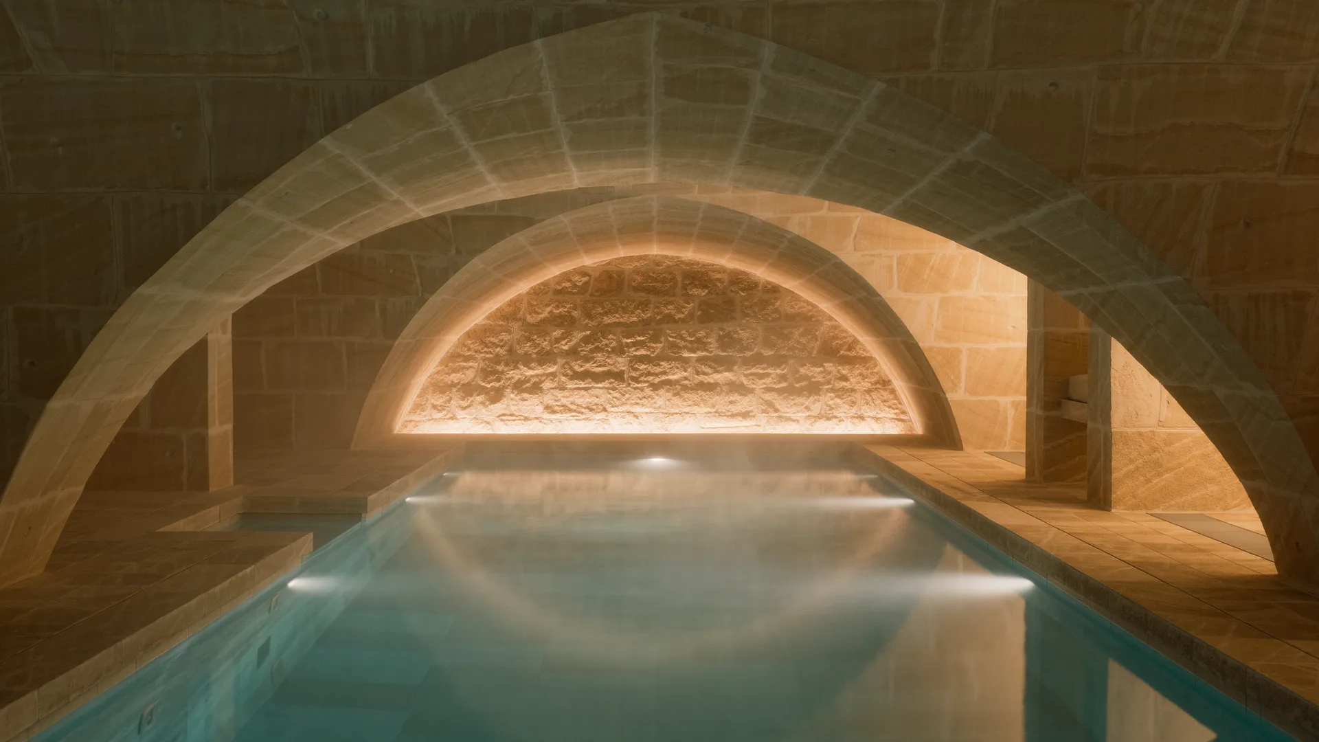 Hotel spa pool lit from below in a stone vaulted room